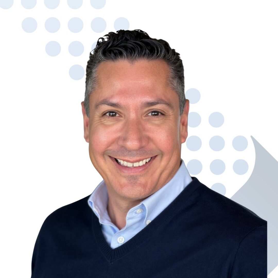 <b>Juan Villasana</b> Smiling man in navy sweater and collared shirt